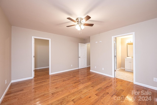 unfurnished bedroom featuring ceiling fan, sink, ensuite bathroom, light hardwood / wood-style floors, and a walk in closet