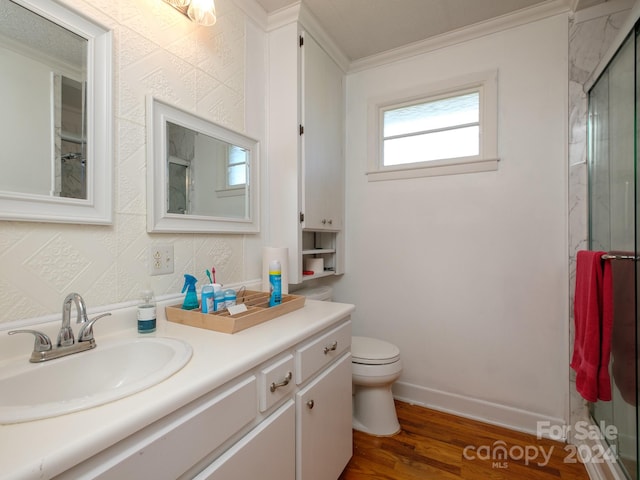 bathroom with crown molding, hardwood / wood-style floors, toilet, a shower with door, and vanity