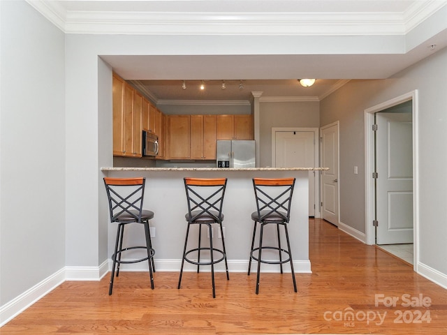 kitchen featuring a kitchen breakfast bar, light hardwood / wood-style flooring, stainless steel appliances, and ornamental molding