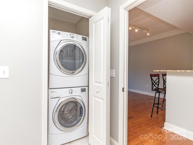 clothes washing area featuring stacked washer and dryer, track lighting, hardwood / wood-style flooring, and ornamental molding