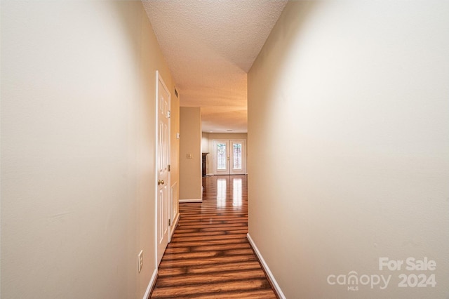 corridor featuring dark hardwood / wood-style flooring, a textured ceiling, and french doors