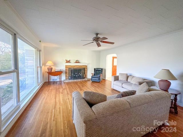 living room featuring crown molding, hardwood / wood-style floors, ceiling fan, and a brick fireplace