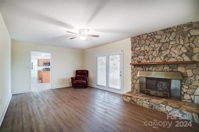 unfurnished living room with a stone fireplace, ceiling fan, and dark wood-type flooring