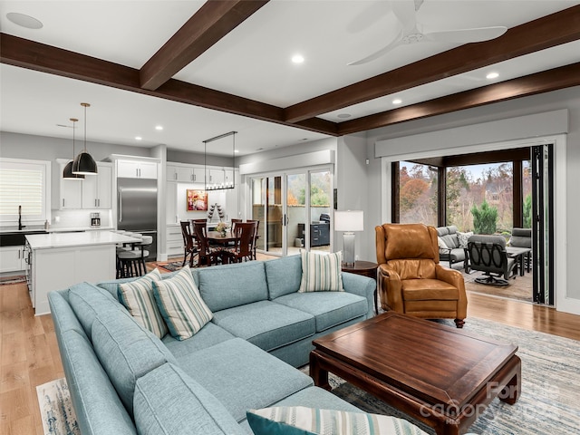 living room featuring ceiling fan, light hardwood / wood-style flooring, and beamed ceiling