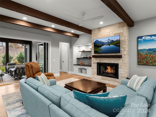 living room featuring beamed ceiling, ceiling fan, a stone fireplace, and light hardwood / wood-style flooring