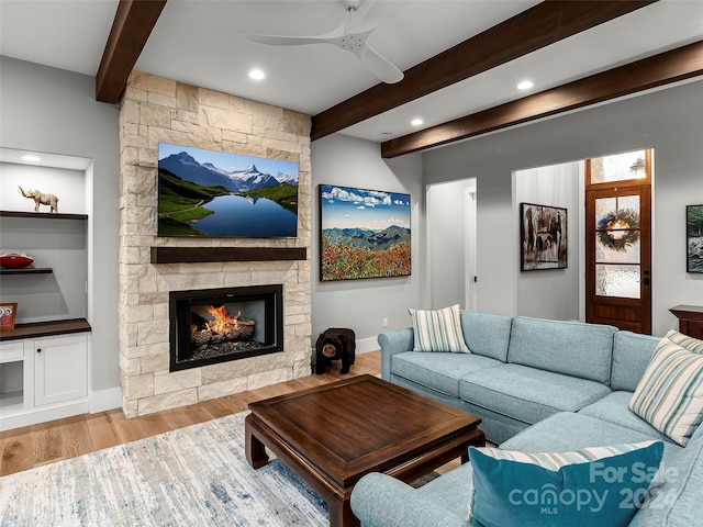 living room with beamed ceiling, ceiling fan, light wood-type flooring, and a fireplace