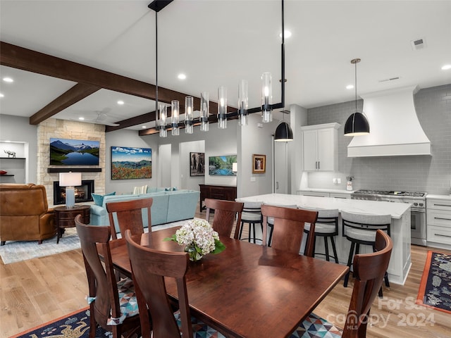 dining area featuring beam ceiling, a stone fireplace, and light wood-type flooring