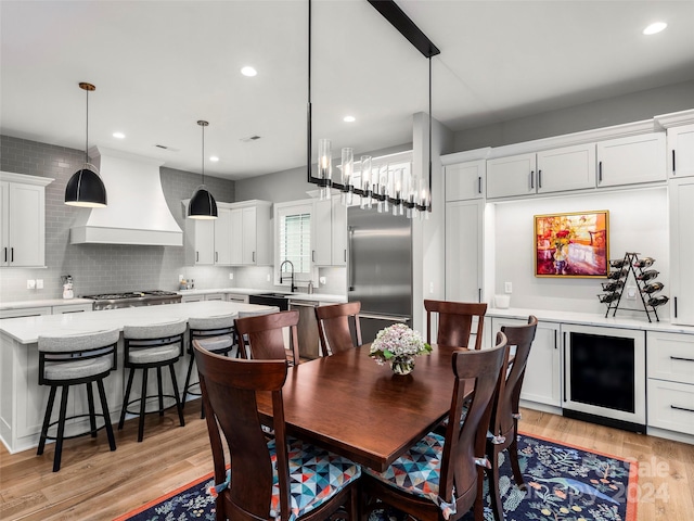 dining space featuring light wood-type flooring, wine cooler, and sink