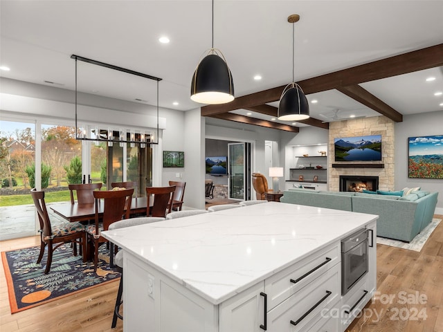 kitchen with light wood-type flooring, white cabinets, a center island, a stone fireplace, and hanging light fixtures