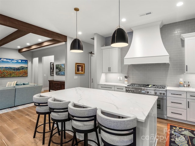 kitchen featuring a center island, premium range hood, range with two ovens, light hardwood / wood-style flooring, and a breakfast bar area