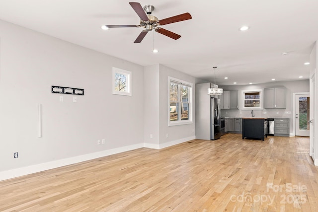 unfurnished living room with sink, ceiling fan with notable chandelier, and light hardwood / wood-style flooring