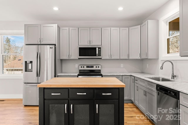 kitchen with sink, light hardwood / wood-style flooring, appliances with stainless steel finishes, gray cabinetry, and a kitchen island