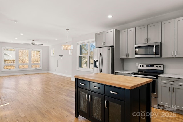 kitchen with stainless steel appliances, a kitchen island, gray cabinets, and butcher block countertops