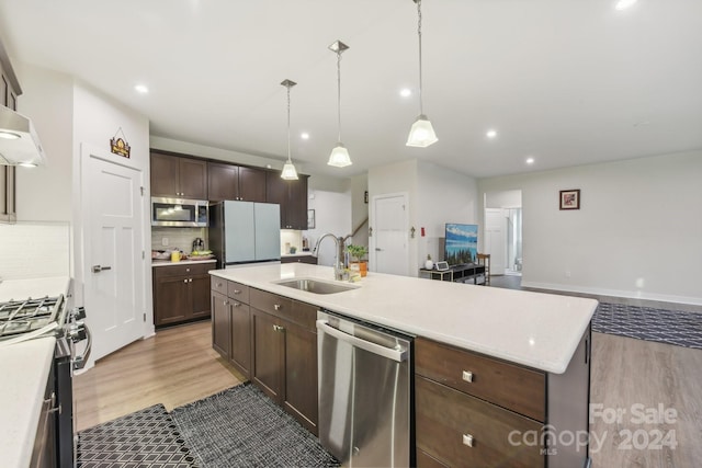 kitchen featuring a kitchen island with sink, sink, light wood-type flooring, decorative light fixtures, and stainless steel appliances