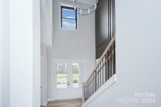 foyer with french doors, light hardwood / wood-style floors, a notable chandelier, and a high ceiling