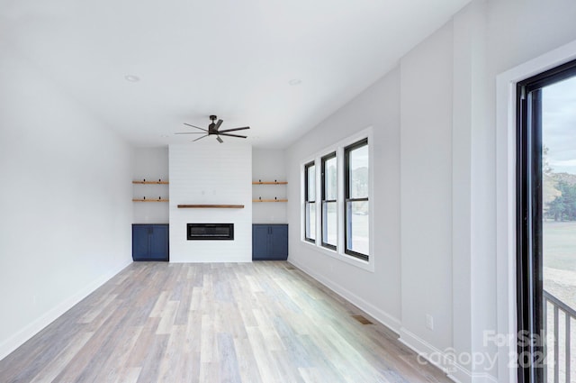 unfurnished living room with ceiling fan, a large fireplace, and light hardwood / wood-style flooring