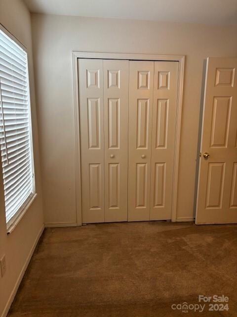 unfurnished bedroom with dark colored carpet, a closet, and multiple windows