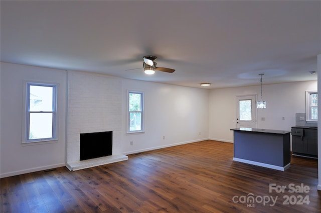 unfurnished living room featuring ceiling fan, dark hardwood / wood-style flooring, a wealth of natural light, and a brick fireplace