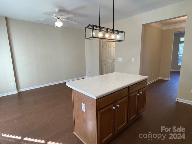 kitchen with ceiling fan, dark wood-type flooring, decorative light fixtures, a kitchen island, and ornamental molding