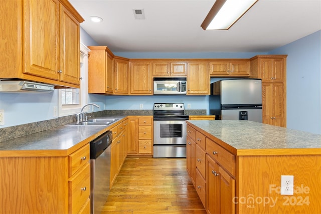 kitchen with appliances with stainless steel finishes, light hardwood / wood-style floors, a kitchen island, and sink