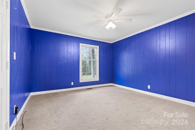 carpeted empty room with ceiling fan, wooden walls, and ornamental molding