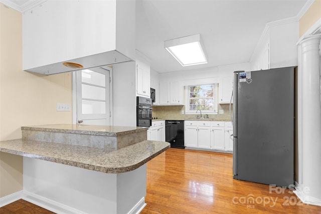 kitchen with sink, kitchen peninsula, white cabinets, black appliances, and light wood-type flooring