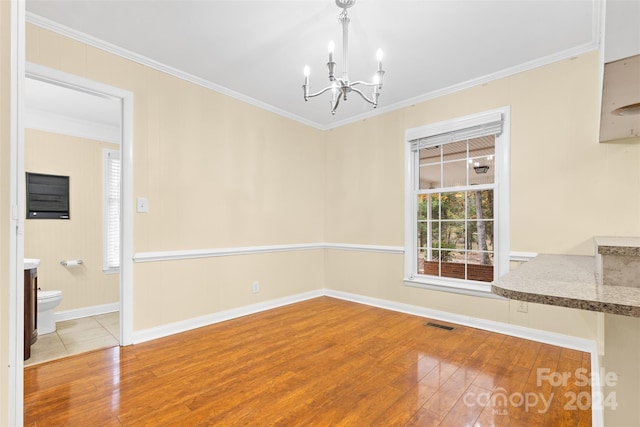 unfurnished dining area featuring hardwood / wood-style floors, crown molding, and an inviting chandelier