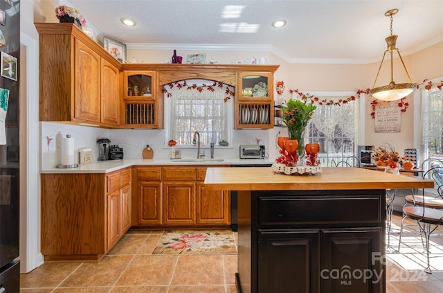 kitchen featuring butcher block countertops, crown molding, sink, and hanging light fixtures