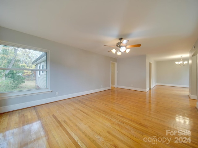 unfurnished room with ceiling fan with notable chandelier and light hardwood / wood-style floors