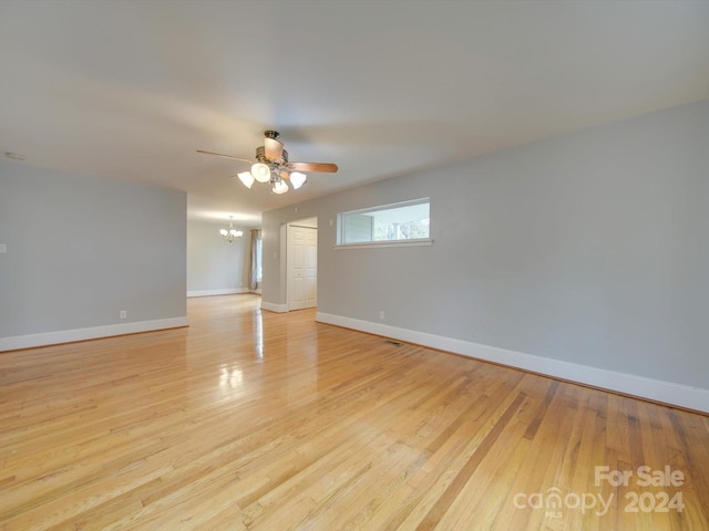 empty room featuring ceiling fan with notable chandelier and light hardwood / wood-style floors