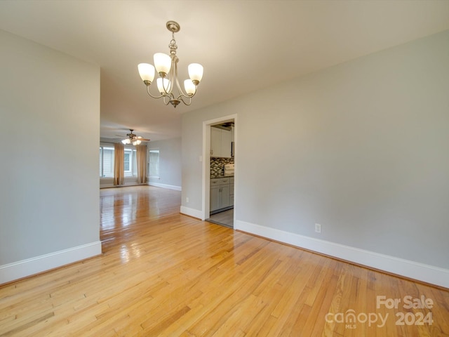 empty room with ceiling fan with notable chandelier and light hardwood / wood-style flooring