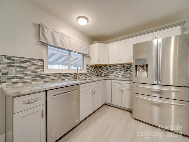 kitchen featuring light stone counters, stainless steel appliances, white cabinetry, and sink