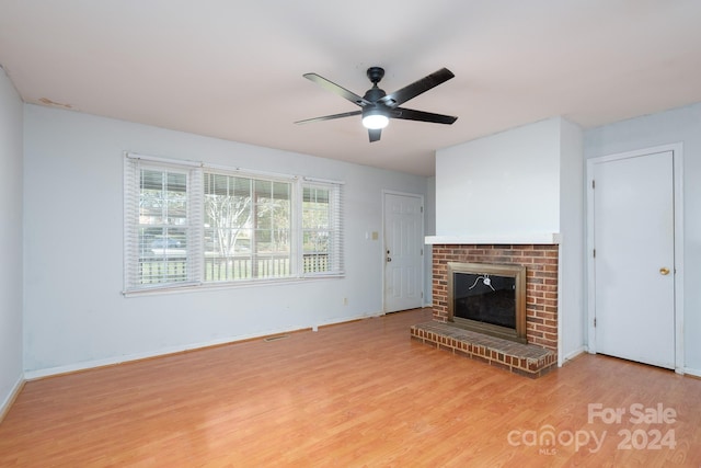 unfurnished living room with light wood-type flooring, a brick fireplace, and ceiling fan