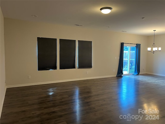 unfurnished room with an inviting chandelier and dark wood-type flooring