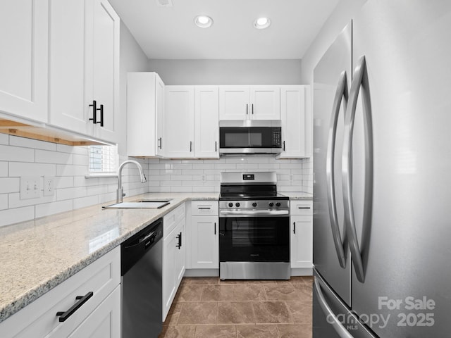 kitchen featuring white cabinets, light stone countertops, appliances with stainless steel finishes, and a sink