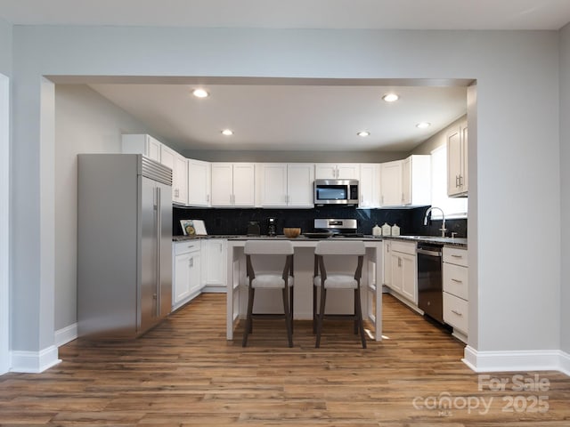 kitchen featuring a kitchen breakfast bar, stainless steel appliances, white cabinets, a center island, and light hardwood / wood-style floors