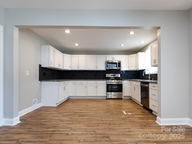 kitchen featuring decorative backsplash, dark stone counters, stainless steel appliances, light hardwood / wood-style floors, and white cabinetry