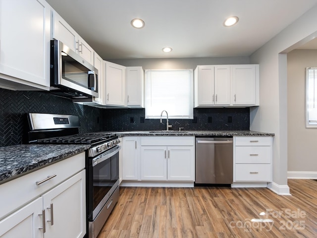 kitchen featuring stainless steel appliances, white cabinetry, dark stone counters, and sink