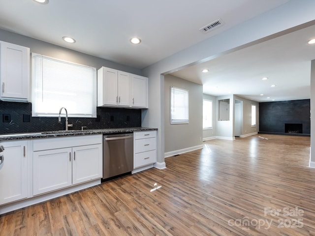 kitchen with dishwasher, white cabinets, sink, light wood-type flooring, and a large fireplace