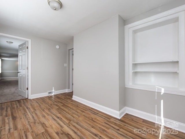 spare room featuring hardwood / wood-style flooring and built in shelves