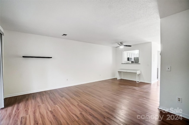 unfurnished living room with a textured ceiling, ceiling fan, and dark wood-type flooring