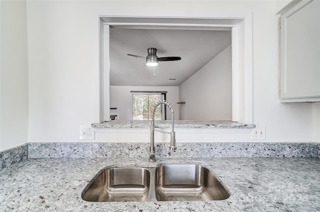 interior details with white cabinetry, sink, ceiling fan, and light stone counters