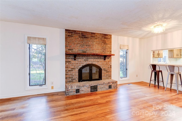 unfurnished living room with light hardwood / wood-style floors, a textured ceiling, and a brick fireplace