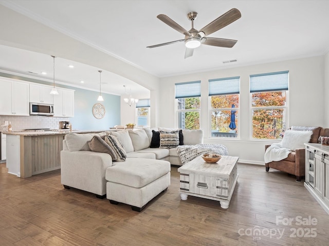 living room with dark hardwood / wood-style flooring, ceiling fan with notable chandelier, and ornamental molding