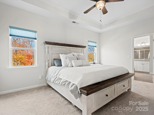 carpeted bedroom featuring ceiling fan, ensuite bathroom, and a raised ceiling