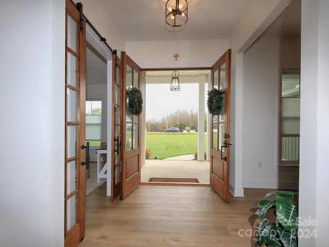 doorway to outside featuring a barn door, a chandelier, french doors, and light hardwood / wood-style floors