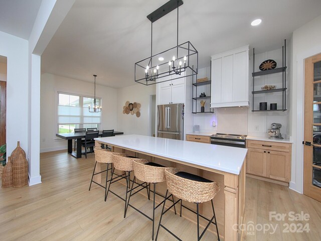 kitchen with a kitchen breakfast bar, stainless steel appliances, light brown cabinets, light hardwood / wood-style flooring, and a kitchen island