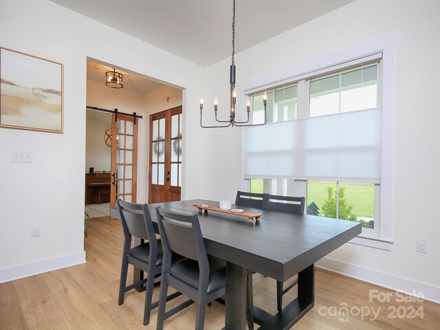 dining area with a notable chandelier, a barn door, a healthy amount of sunlight, and light hardwood / wood-style flooring