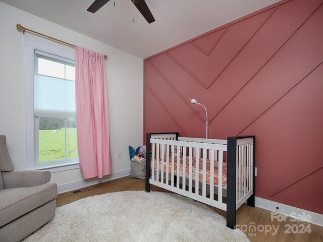 bedroom featuring hardwood / wood-style floors, ceiling fan, a crib, and multiple windows