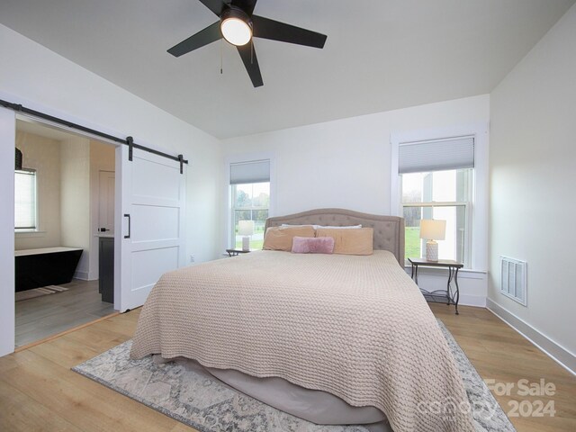 bedroom with a barn door, ceiling fan, and light hardwood / wood-style floors